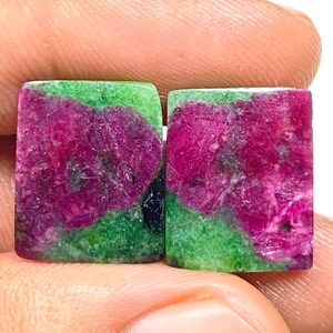 Può includere: Due pietre preziose rettangolari con una vibrante combinazione di colori. Le pietre presentano uno straordinario contrasto di tonalità magenta intenso e verde lussureggiante. Le aree magenta hanno un aspetto strutturato, mentre le aree verdi appaiono lisce. Queste pietre sono ideali per la gioielleria.