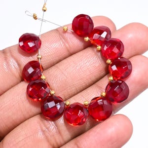 May include: Strung faceted red gemstone beads with gold-colored spacers. The beads are a deep, transparent red, and the facets catch the light. The beads are strung on a thin, clear wire.