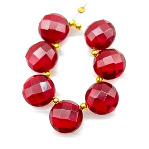 May include: Strand of faceted, round, deep red beads with gold-colored spacer beads. The beads are strung on a thin, clear wire. The beads have a shiny, reflective surface and are set against a white background.