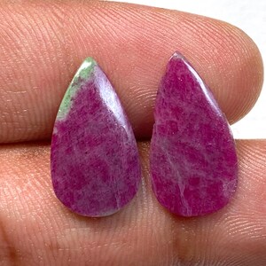 Może przedstawiać: Dwa oszlifowane kamienie szlachetne w kształcie łezki. Mają głęboki, purpurowy kolor z subtelnymi białymi żyłkami i odrobiną zieleni na czubku jednego z nich. Prawdopodobnie do wyrobu biżuterii.