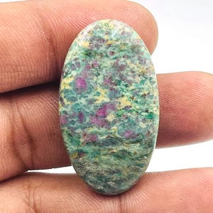 May include: An oval-shaped gemstone with a mottled pattern of green, yellow, and deep pink hues. The polished surface of the stone displays a mix of colors and textures, creating a unique appearance. The gemstone is held in a hand.