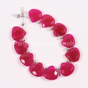 May include: A strand of faceted, heart-shaped fuchsia gemstones arranged in a curved line, separated by small, round, metallic silver beads. The text PanjatanGemsJewels is overlaid in white across the center of the gemstone strand.