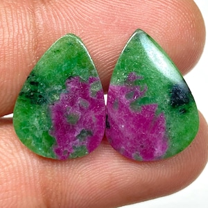 Może przedstawiać: Dwa kamienie szlachetne w kształcie łezki. Każdy kamień ma zieloną podstawę z magentowymi i czarnymi wtrąceniami. Wypolerowane kamienie ukazują naturalne wzory.