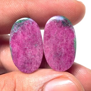 Può includere: Due gemme ovali di un vibrante colore rosa, accentuate da striature verdi e bianche. Le pietre lucide sono tenute in una mano, mostrando le loro superfici lisce e riflettenti. Queste gemme sono ideali per la creazione di gioielli.