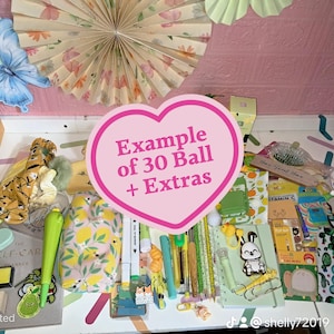 May include: A selection of stationery and accessories, including notebooks, pens, stickers, and decorative items. The image features a variety of colours and patterns, with a heart-shaped graphic that reads "Example of 30 Ball + Extras".