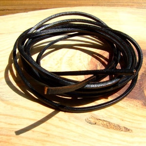 Puede incluir: Un rollo de cordón de cuero negro, de aproximadamente 6 mm de grosor, se muestra sobre una superficie de madera.