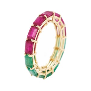 Peut inclure: Une bague en or ornée de sections alternées de pierres précieuses roses et vertes de coupe rectangulaire. Les pierres sont serties dans une monture en or, créant un design coloré et élégant. La bague est présentée sur fond blanc.