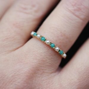 May include: A gold ring featuring alternating turquoise and white pearl-like beads. The ring is displayed on a finger, highlighting the delicate design and colour contrast. The ring is a piece of jewellery.