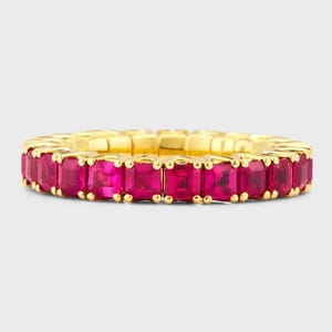 Peut inclure: Une bague dorée ornée d'une rangée continue de pierres précieuses roses rectangulaires. Les pierres sont rapprochées, formant un design complet et saisissant. La bande de la bague a une finition lisse et polie.
