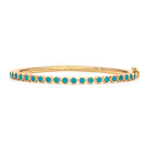 May include: A gold-coloured bangle bracelet featuring a line of small, round turquoise stones. The bracelet has a simple, elegant design and a clasp closure. The turquoise stones are evenly spaced around the bracelet.