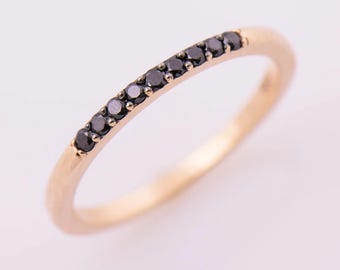 May include: A gold ring featuring a line of small, black gemstones. The ring has a smooth, polished surface and a slender band. The gemstones are evenly spaced, adding a subtle sparkle. The ring's design is simple yet elegant.