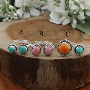 May include: Three open-style silver rings labeled A, B, and C. Ring A features two small turquoise stones. Ring B has two oval pink stones. Ring C displays a large round orange stone paired with a smaller turquoise stone, all in silver settings.