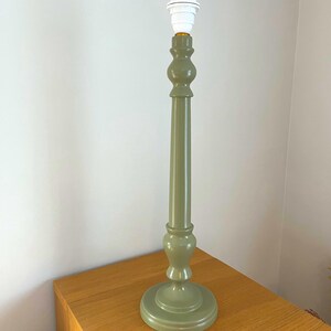 May include: A sage green table lamp base with a white bulb socket. The lamp has a round base, a long, slender stem, and decorative bulbous sections. The lamp is placed on a wooden surface.