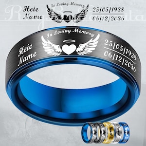 May include: A blue and black stainless steel ring with the text "Heie Name" and "In Loving Memory". The ring features a heart with wings and the dates 25/05/1938 and 06/12/2036. Several other rings in different colours are visible.