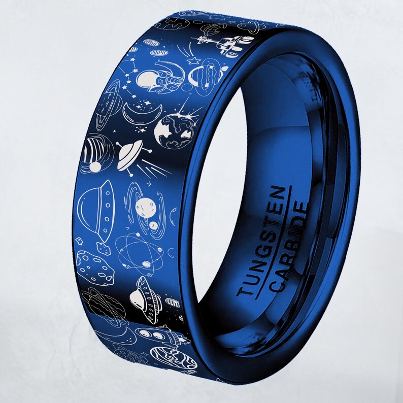 May include: A blue tungsten carbide ring with a space-themed design. The ring features white line drawings of planets, rockets, and other space elements. The text "TUNGSTEN CARBIDE" is printed on the side of the ring.