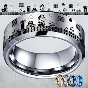 Puede incluir: Un anillo plateado con un diseño grabado en negro que representa un videojuego. El diseño incluye un personaje, nubes y otros elementos del juego. El anillo tiene un acabado pulido y un interior liso.