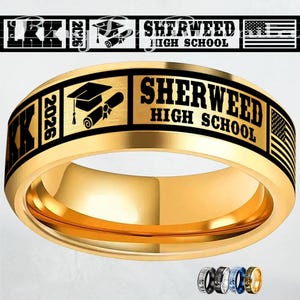 Könnte beinhalten: Ein goldfarbener Ring mit schwarzen gravierten Texten und Grafiken. Der Ring trägt die Aufschrift "SHERWEED HIGH SCHOOL" und "2026". Eine Abschlusskappe und ein Diplom sind ebenfalls eingraviert. Der Ring hat eine glänzende, polierte Oberfläche.