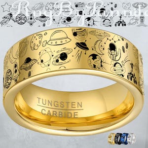 Könnte beinhalten: Ein goldfarbener Wolframkarbid-Ring mit einem detaillierten schwarzen Strichdesign von Planeten, Raketen und Weltraumelementen. Der Ring trägt die Gravur "Tungsten Carbide". Der Ring ist im Bandstil gehalten.