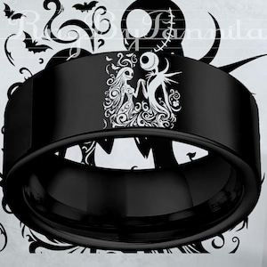 May include: A black ring with a white graphic of a couple holding hands. The ring has a wide band and a polished finish. The design features a man with a round head and a woman with long hair, both in a gothic style. The ring is likely made of metal.