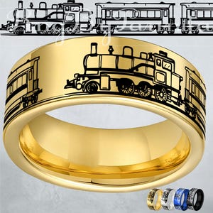 May include: A gold-colored ring with a black train design wrapping around the band. The ring features a detailed illustration of a train engine and passenger cars. The ring is shown with four other color options.