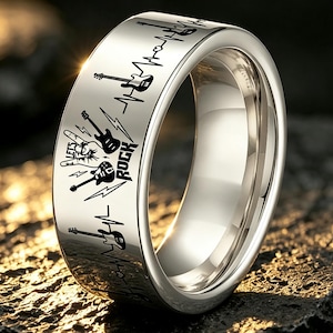 May include: A polished silver-toned metal ring featuring a laser-engraved design of electric guitars, a hand making a rock-and-roll gesture, lightning bolts, and a heartbeat line. The text "LETS ROCK" is clearly visible on the outer band surface.