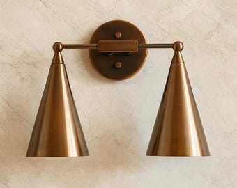 May include: A bronze-toned wall sconce with two conical shades. The fixture has a circular backplate and a horizontal bar connecting the shades. The sconce is mounted on a marble-patterned wall, offering a vintage aesthetic.