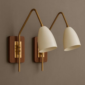 May include: A pair of wall sconces in a mid-century modern style. Each has a cream-coloured, cone-shaped shade, a brass arm, and a rectangular wooden base. The sconces are mounted on a neutral-coloured wall.