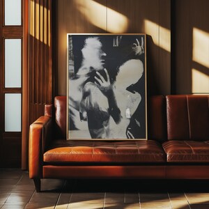 May include: A framed black and white art print featuring an abstract image of two figures. The artwork is displayed above a brown leather sofa. The room has wooden paneling and a door with rectangular glass panels.