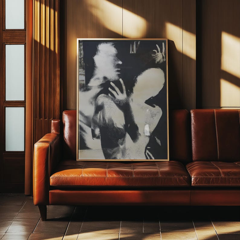 May include: A framed black and white art print featuring an abstract image of two figures. The artwork is displayed above a brown leather sofa. The room has wooden paneling and a door with rectangular glass panels.