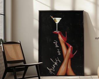 May include: A framed art print featuring a martini glass balanced on a pair of legs wearing red high heels. The artwork has the words "Drinks on me" in a cursive font against a black background.