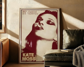 May include: A framed art print with a red and cream portrait of Kate Moss. The words "IT GIRL" and "KATE MOSS" are printed in bold text. The artwork is displayed in a living room setting, next to a leather sofa.