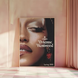 Op de afbeelding: Een ingelijste poster met een close-up van een gezicht, rode lippenstift en een rode oorbel. De poster toont de tekst "Vivienne Westwood" en "Spring 1998" in het wit.