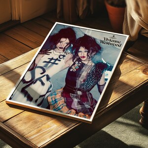 Peut inclure: Une impression encadr&eacute;e pr&eacute;sentant deux personnes dans une mode avant-gardiste. L'impression affiche le logo Vivienne Westwood. Les sujets portent des tenues uniques avec un maquillage et des coiffures audacieux. L'impression est pos&eacute;e sur une surface en bois.