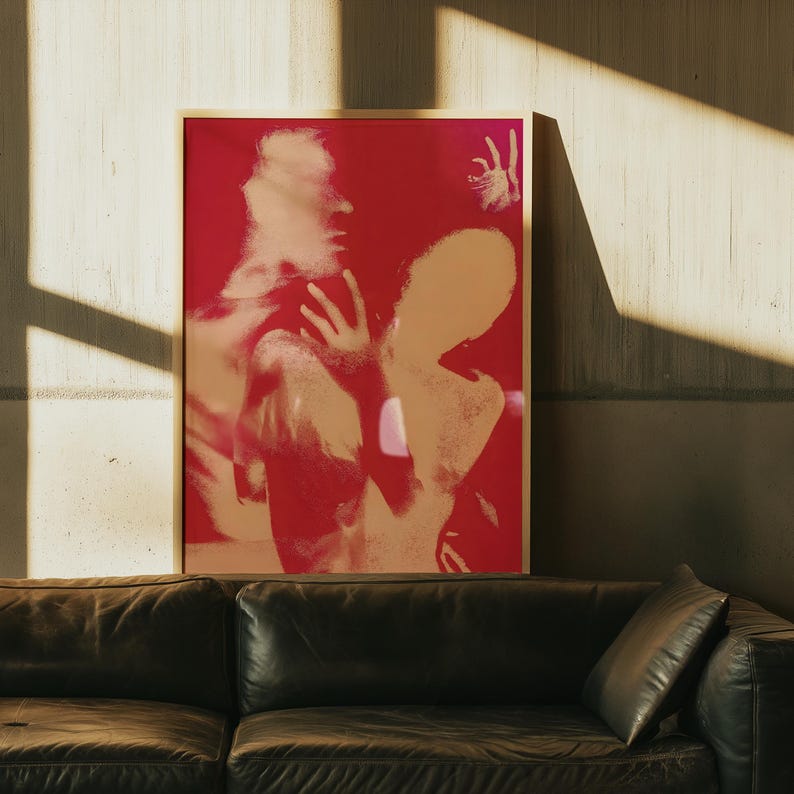 May include: A framed art print featuring a red and beige abstract image of two figures. The artwork has a modern aesthetic, with a focus on form and color. The print is displayed on a wall, with a leather sofa in the foreground.
