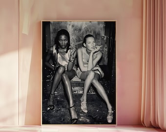 May include: Black and white framed photograph featuring two women seated, each holding a cigarette. They are wearing dresses and heels. The photograph is displayed in a room with pink walls and a checkered floor.