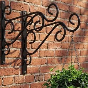 May include: Black wrought iron plant hanger with decorative scrollwork, mounted on a red brick wall. A hanging basket with green foliage is suspended from the hook. The hanger is designed to hold a potted plant.