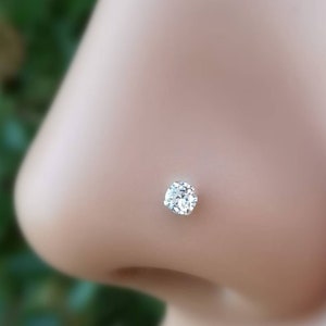May include: A close-up of a clear nose ring with a small, round, clear gemstone.