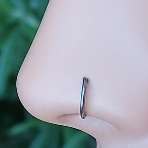 May include: A close-up of a silver nose ring hoop on a mannequin's nose. The ring is simple and understated, with a smooth finish.