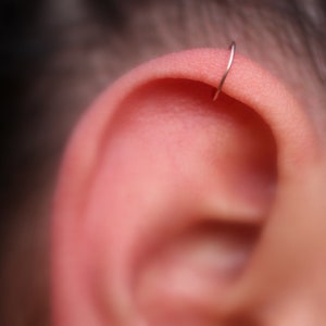 May include: Close-up of a person's ear with a small, silver hoop earring in the upper cartilage.