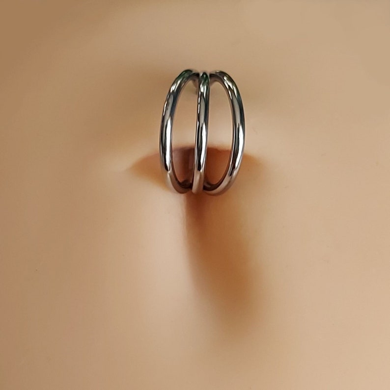 May include: A silver belly button ring with a triple hoop design.