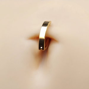 May include: A gold belly button ring with a flat, smooth, and slightly curved bar.