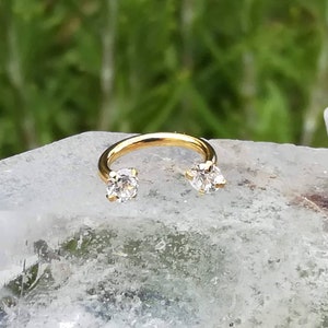 May include: Gold horseshoe shaped earring with two clear cubic zirconia stones.
