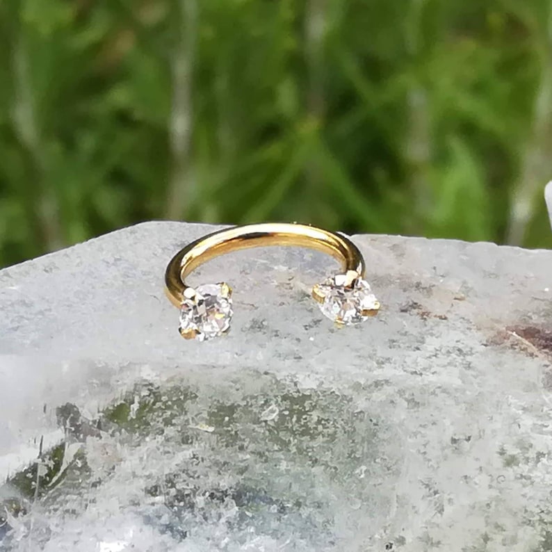 May include: Gold horseshoe shaped earring with two clear cubic zirconia stones.