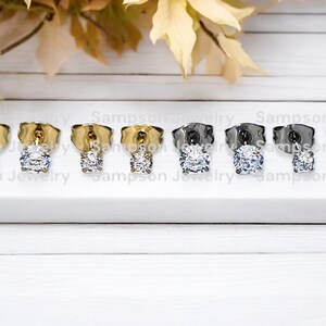 May include: Six pairs of earrings with a clear round stone. The earrings are in three different metal finishes: gold, silver, and black.