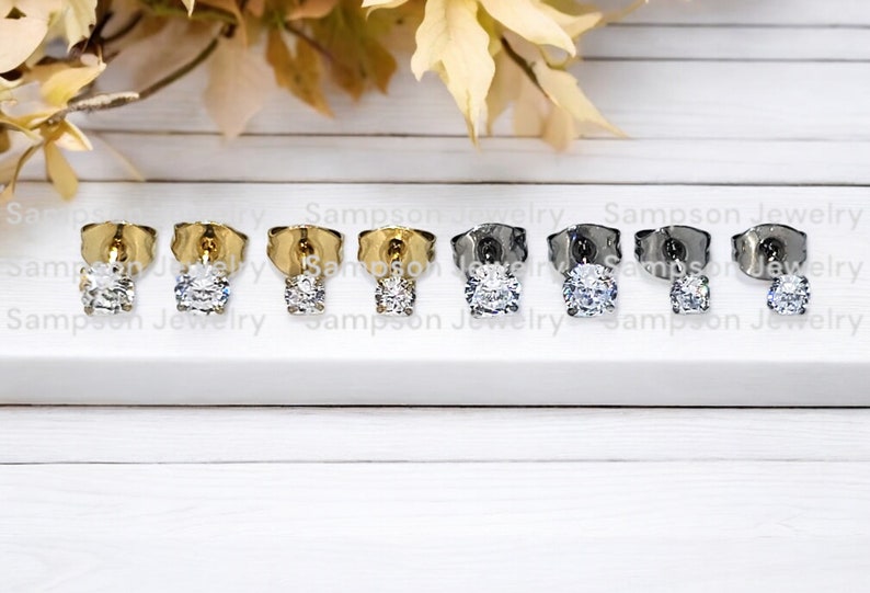 May include: Six pairs of earrings with a clear round stone. The earrings are in three different metal finishes: gold, silver, and black.