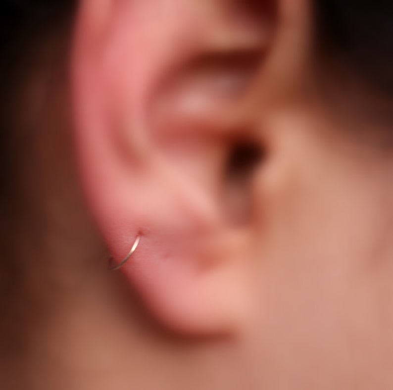 May include: A close-up of a person's ear with a small silver hoop earring.