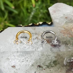 May include: Two 6mm horseshoe rings with clear gemstones. The ring on the left is gold and the ring on the right is silver.