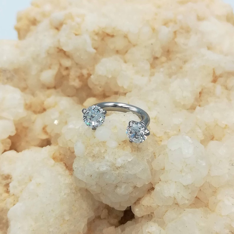 May include: A silver circular barbell with two clear round cubic zirconia stones.