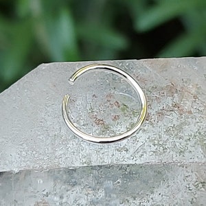 May include: A silver nose ring hoop, a type of body jewelry, is shown on a white background.