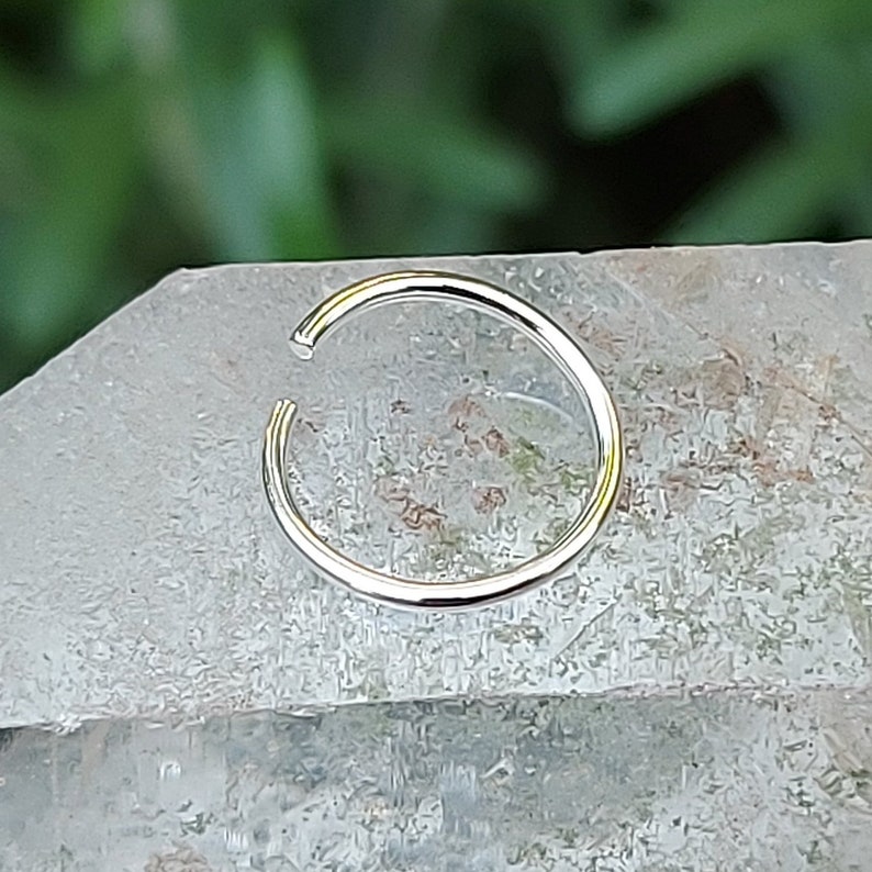 May include: A silver nose ring hoop, a type of body jewelry, is shown on a white background.